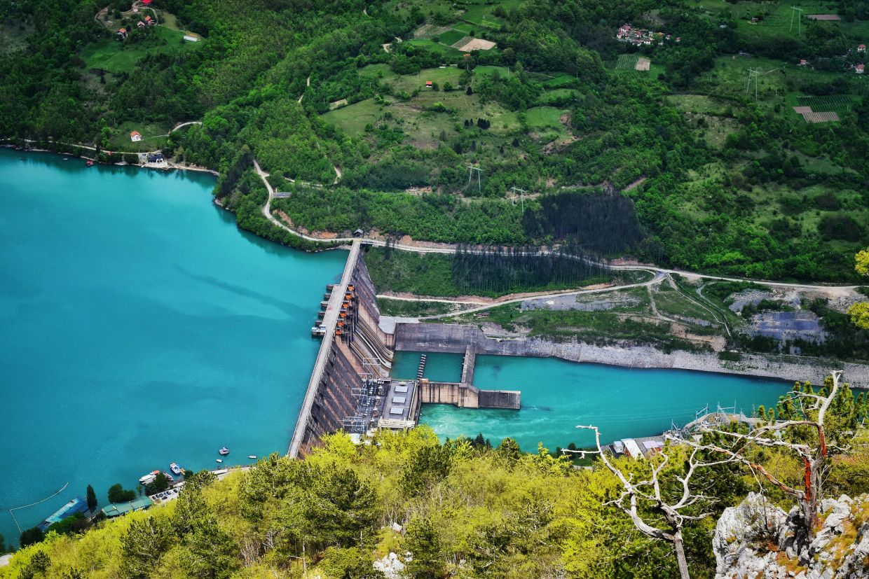 Presa de una central hidroeléctrica con el embalse lleno y el agua saliendo por los aliviaderos en un valle de España